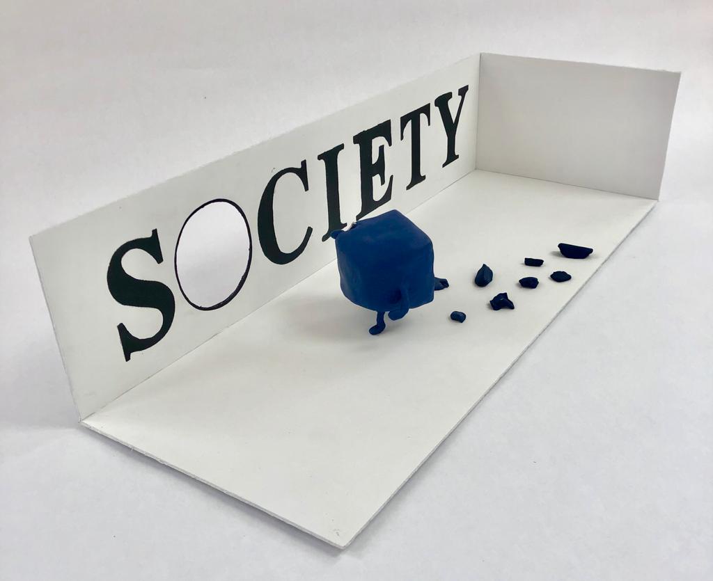 3D sculpture of a cube chipping away its corners to fit into society, which is written on the wall with a circular hole.